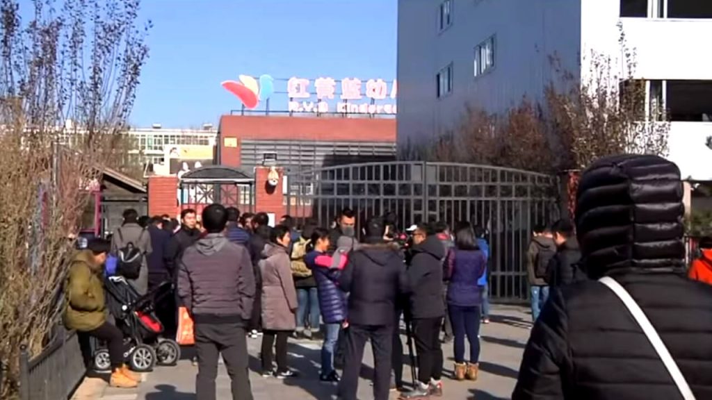 People stand in front of the main gate of the RYB New World Kindergarten in Beijing's Chaoyang district. 
