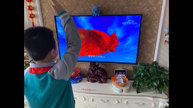 A primary school student gives a salute while watching a flag-raising ceremony on online class through TV at home in Shandong’s Jiaozhou city.
