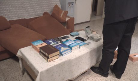 Police officers take photos of faith-related books and other items confiscated in a CAG believer’s home.