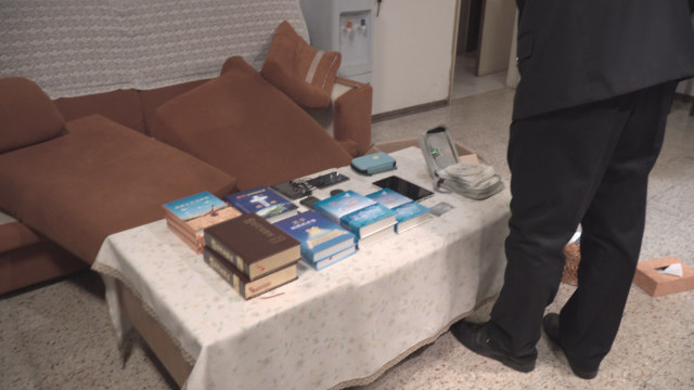 Police officers take photos of faith-related books and other items confiscated in a CAG believer’s home.